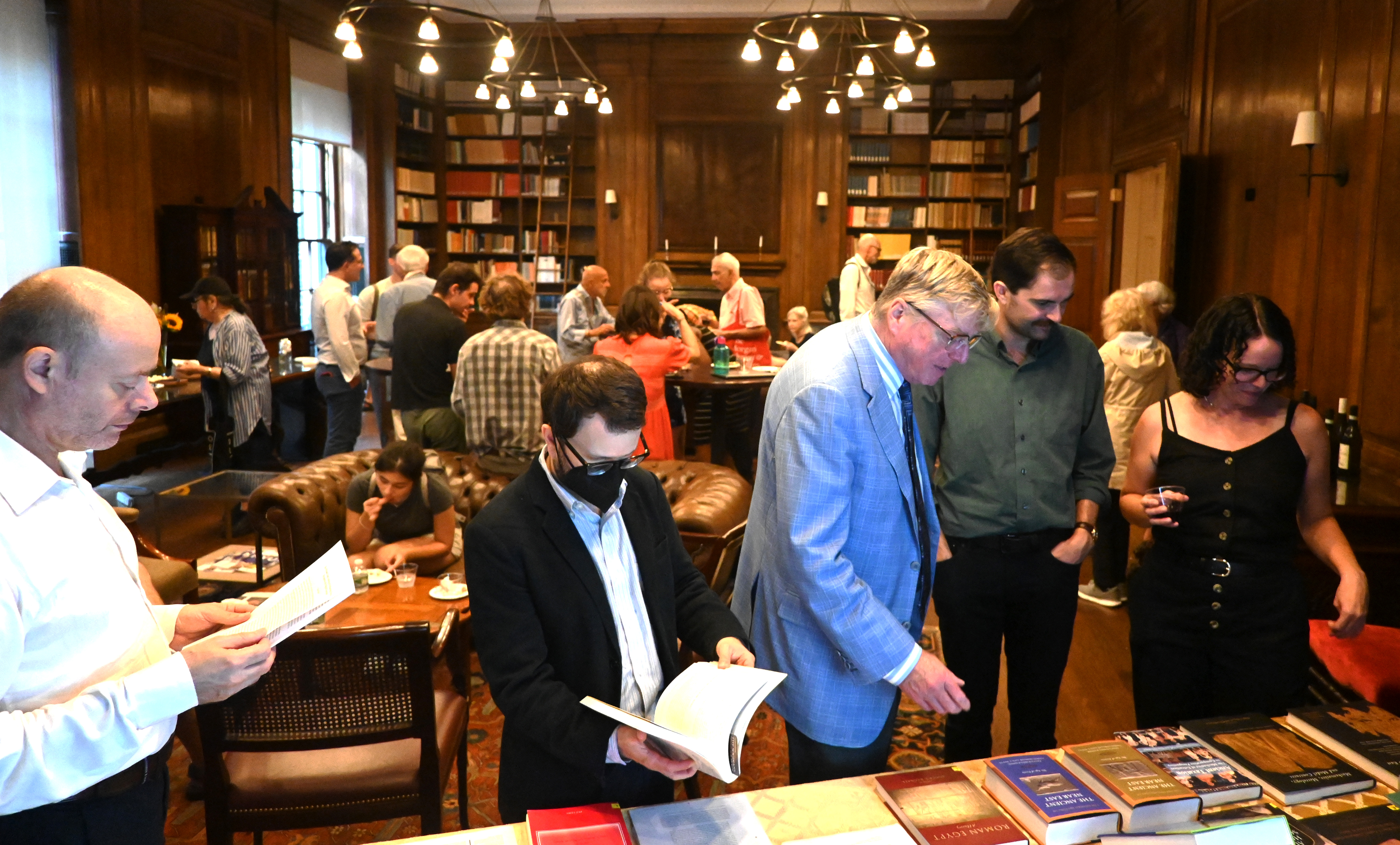 Several attendees of the publication reception mingling in ISAW's Oak library and a smaller group of people checking out the books on display