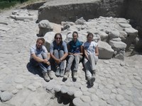 Four archaeologists pose, seated, for a photograph amid an excavated, paved room.