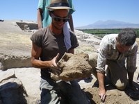 Group of three workers at archaeological site with mountain in background.