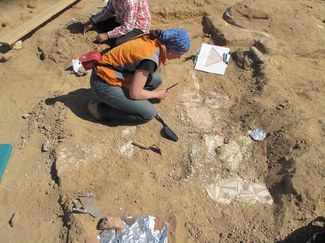 Archaeologist bending over painted plastic fragments on the ground to study, record, and preserve them.