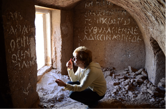 Raffaella Cribiore crouched on the ground studying ancient white writing on walls of an ancient tomb.