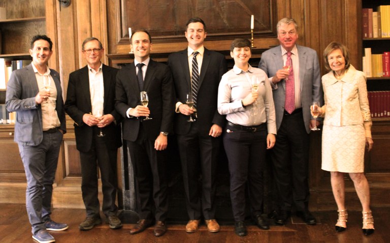 Seven individuals posing in front of a fireplace in a formal library