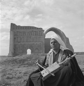 A man sits in front of the ruins of an ancient building while playing an instrument