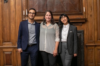 Three individuals pose in front of a fireplace in a formal library