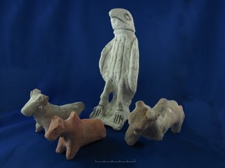 Photograph of a stone statue of a hawk, together with three other stone or ceramic objects that appear to be cattle.