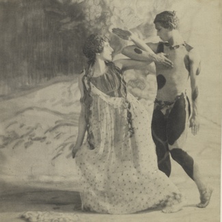 A vintage photograph in black and white depicting two dancers in costume with their arms intertwined