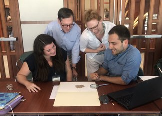 Four people gather around and examine a papyrus fragment on a table.