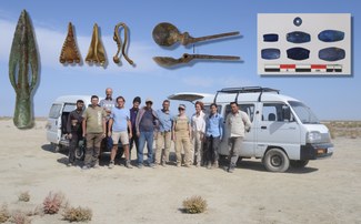Eleven people standing in a rough line in front of two vans in the middle of a desert landscape. Images of various objects (including things that look like a metal spear point and a metal spoon) superimposed on the sky above their heads. 