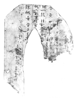 A black-and-white image of a document bearing vertical lines of Chinese characters. Its top corners are rounded and there is an oblong section missing from the middle of the document. Both of the trailing sides are torn off at the bottom.