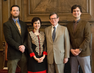 Four people in semi-formal attire stand in a wood panelled room, smiling for the camera.