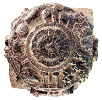 A circular ceramic or stone object with illustrations in relief. In the center, a stylized floral bloom. In the band around the enter, there are depictions of elephants and other animals, tools, anod other objects and figures.