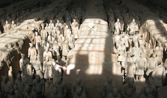 This photograph shows large numbers of ceramic human figures in linear groups in excavated pits, with balks of earth between each.