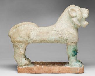 In this photograph, we see from the side a standing, roaring lion made of ceramic and covered in a white glaze.