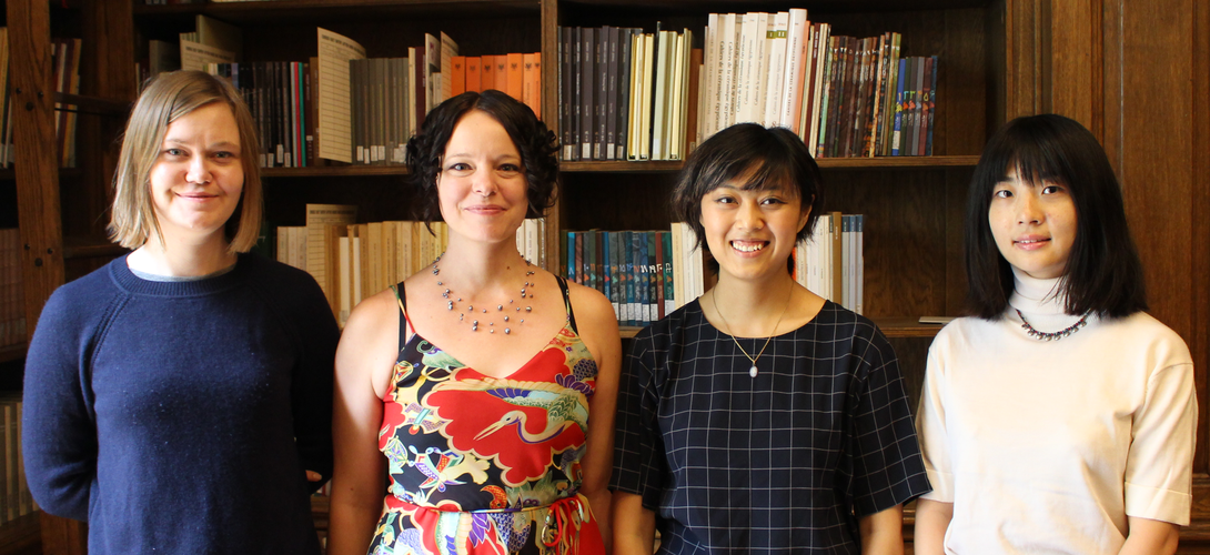 Four women stand and pose for a photograph in a wood-paneled room with bookshelves.