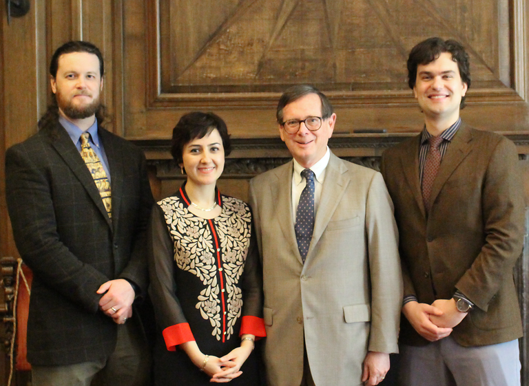 Four people in semi-formal attire pose for a photograph in a wood-paneled room.