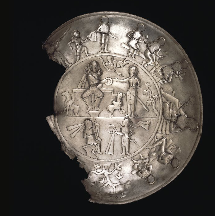 A silver plate, missing part of its left rim and illustration band. A band of figures in relief performing various tasks follows the circumference of the plate. In the center, more figures together with plants and animals appear.