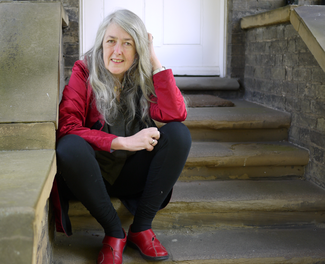 A woman in a red shirt and black slacks sits on a stone stair and looks into the camera.