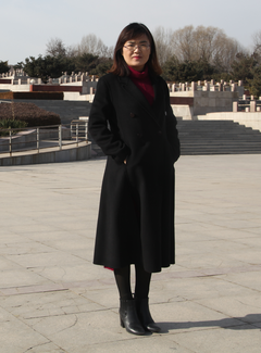 A woman poses in front of what appears to be a monumental stone or concrete plaza and raised area behind.