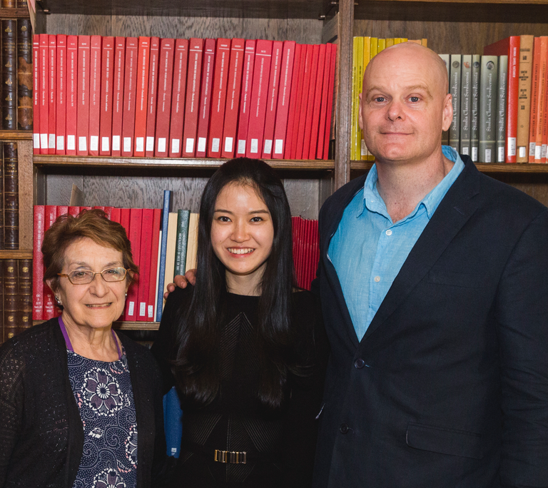 Three people pose for photograph in front of a bookshelf.