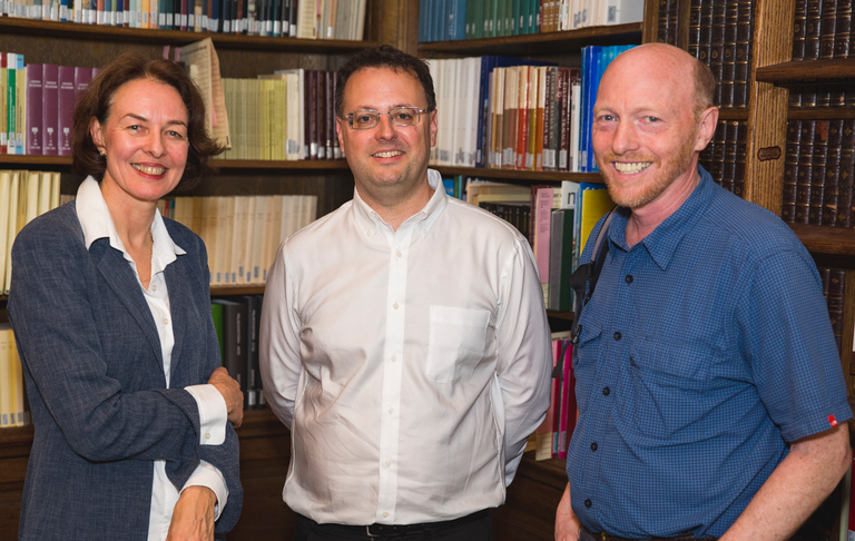 Three people pose for a photograph in front of a corner of a room full of bookshelves.