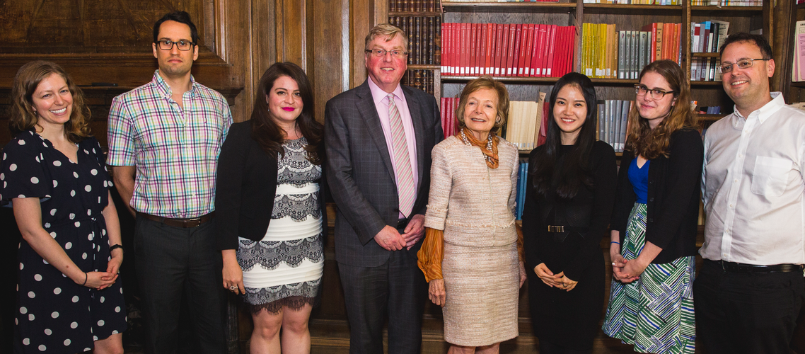 Eight people pose for the photo in a room with bookshelves and wood paneling.