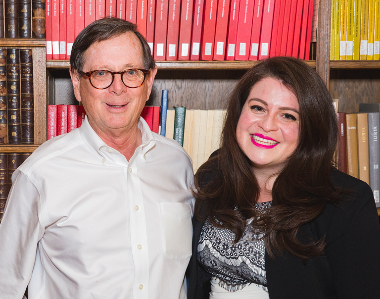 Two people pose for a photo in front of a bookshelf.