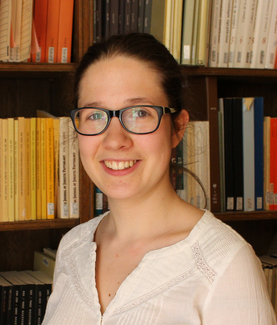 A woman with glasses poses for the camera in front of a bookshelf.