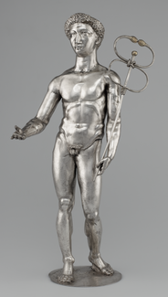 A silver satuette depicting a nude male form holding out his right arm and, in his left hand, grasping a long, narrow wand that ends in two loops, each terminating in a snake head.