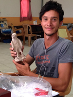 Andrea Trameri poses, seated in a work room, holding a small stone statuette of an eagle.