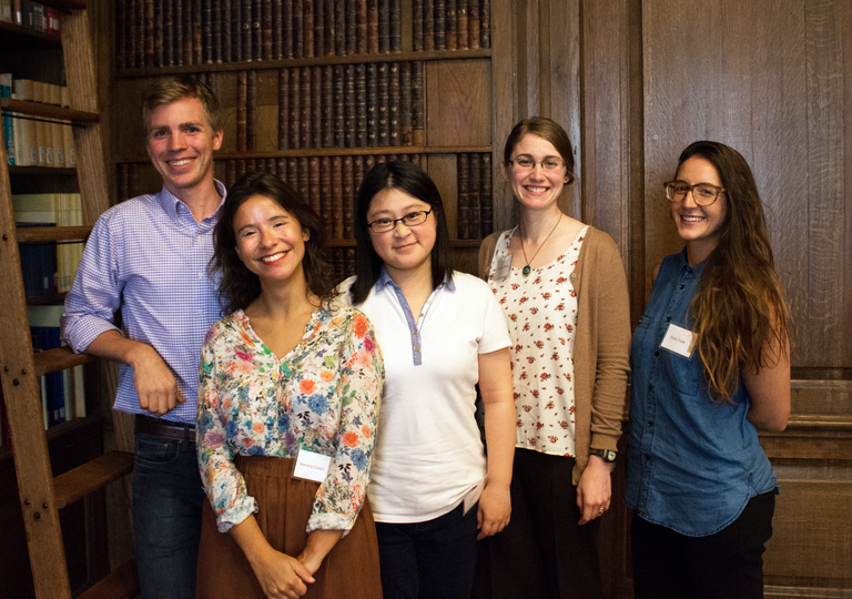 Five people stand and pose for the camera in a room with wood paneling and bookshelves.