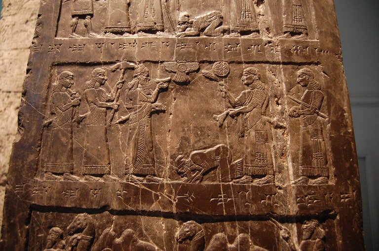 A stone relief depicts multiple human figures in parts of three horizontal groupings.