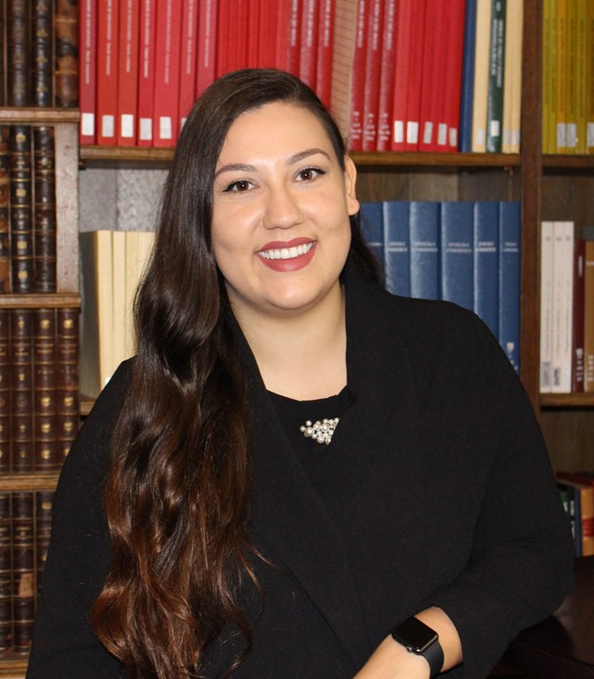 A woman poses for a photograph in front of a book case.