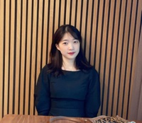 woman sits at table in front of slatted wood paneling