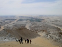 Photo showing the general situation of Amheida taken from a height with people in silhouette in the foreground and the landscape of the Dakhleh oasis stretching away to the horizon in the background