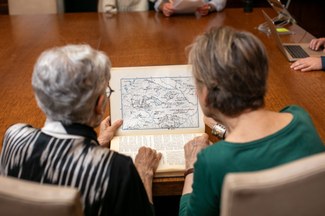 two women from behind point at map.