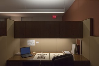 Photograph of a typical scholar's carrel, showing lighting, a laptop, a large gook, storage cabinet, and chair.